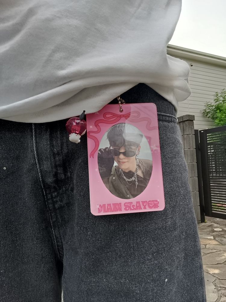 A photocard of jeong yunho (ateez) in a pink photocard holder, hanging off the front belt loop of my jeans