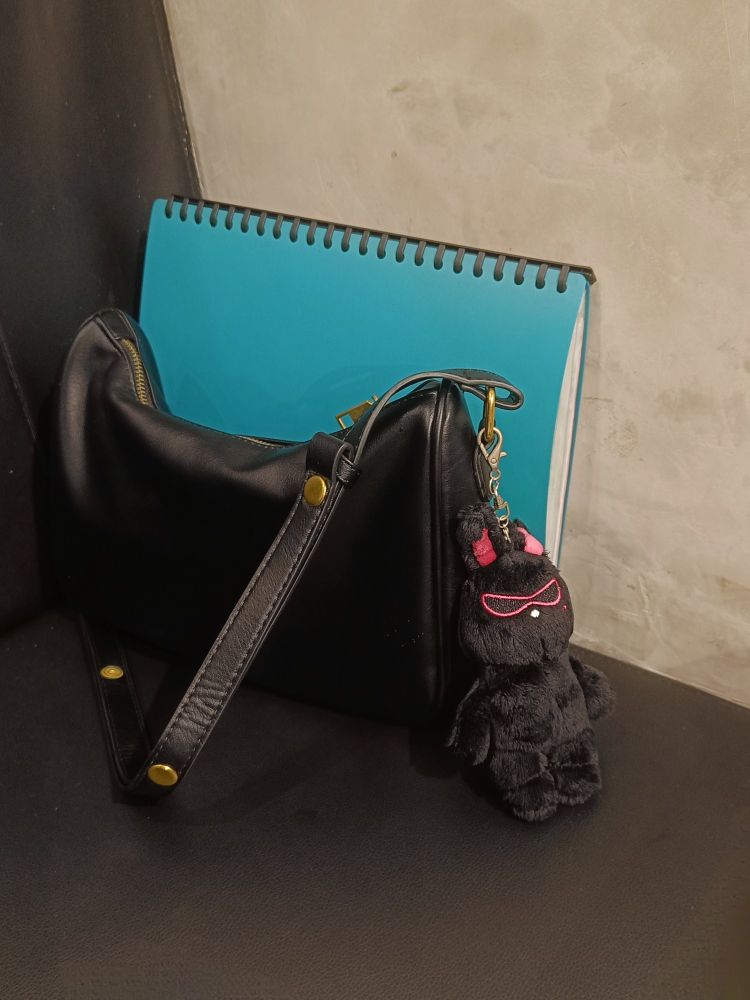 A black bag with an ATEEZ Mito keyring plushie, and a green clear book behind it. They are placed on a black leather(?) seat.