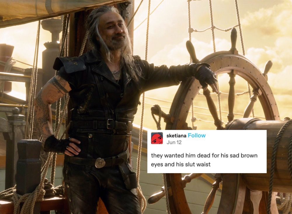 Ed Teach in his leathers standing with one hand on his hip and the other resting on the ship’s wheel. He’s smiling slightly but his eyes look sad. (Season 2 episode 2 of Our Flag Means Death.) A text post by sketiana has been added to the image, it reads: they wanted him dead for his sad brown eyes and his slut waist.