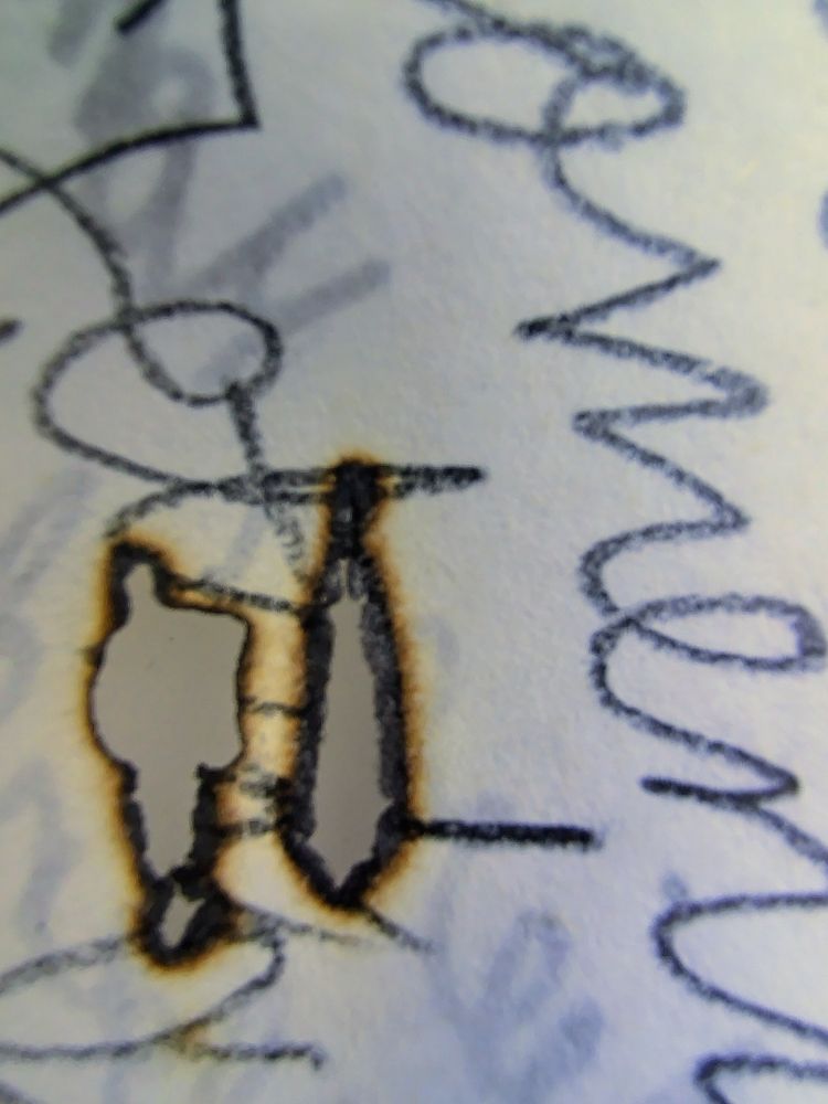 Nahaufnahme von zwei schmalen Brandlöchern auf einem Blatt Papier mit einer krakeligen Kinderhandschrift.