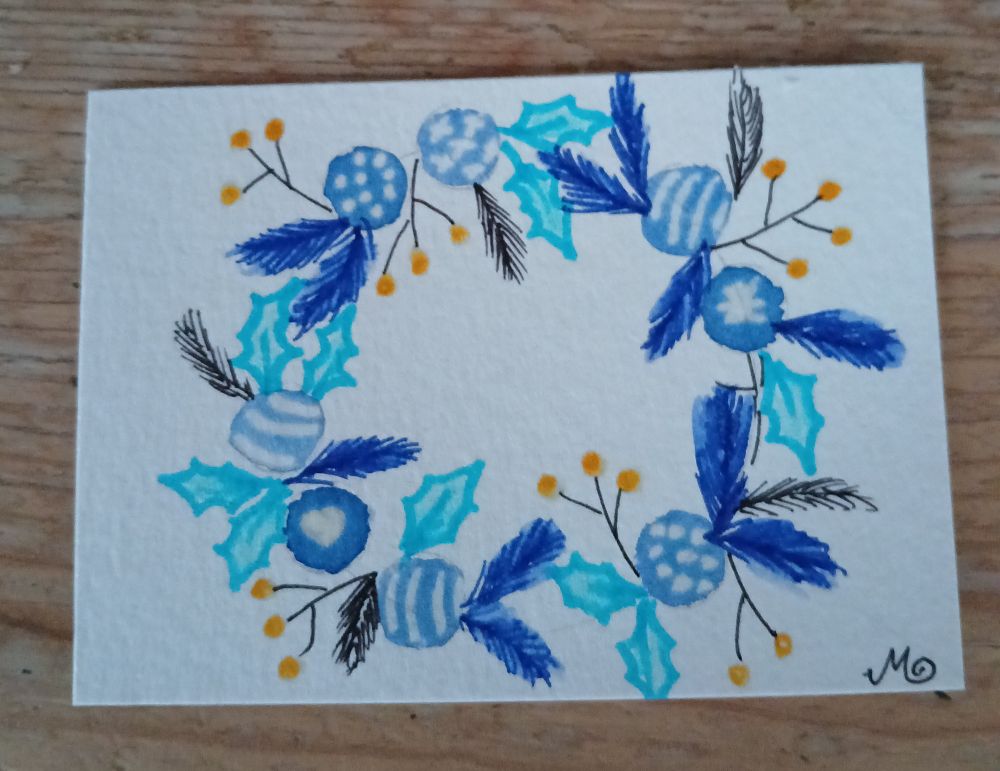 Eine ATC im Querformat auf einem Holztisch. Die Karte zeigt einen Kranz. Gemalt in blau, türkis, orange und schwarz.