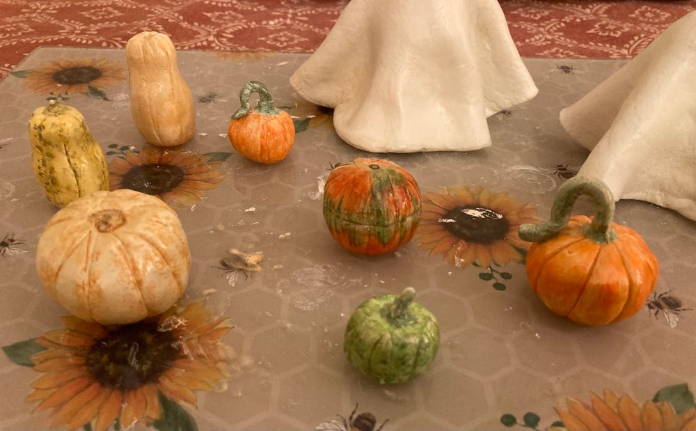 Seven tiny air dry clay pumpkins, including butternut squash, harlequin squash, and pumpkins in shades of orange, green and yellow.
