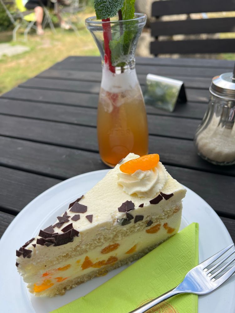 Ein Gartentisch mit einem Stück Sahne-Mandarinen-Torte, grüner Serviette und einer Fancy Limo.