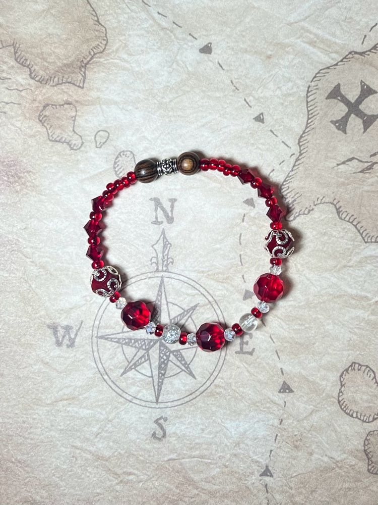 A beaded bracelet inspired by the character Spanish Jackie from Our Flag Means Death. It is comprised of red and clear crystal beads, as well as two wood beads representing her wooden hand.