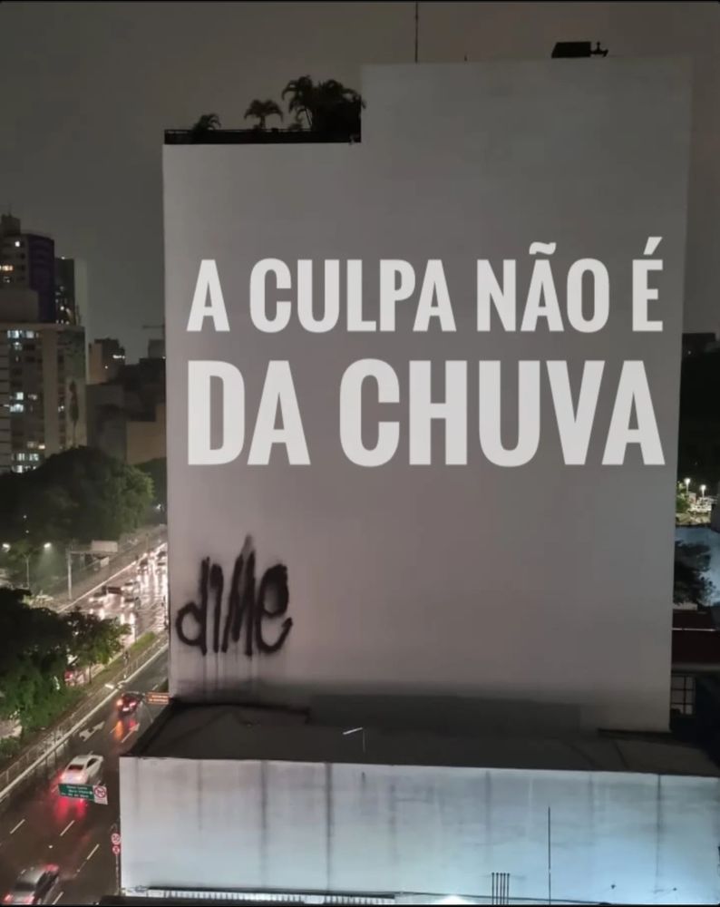 Foto de uma parede de prédio com a projeção A CULPA NÃO É DA CHUVA