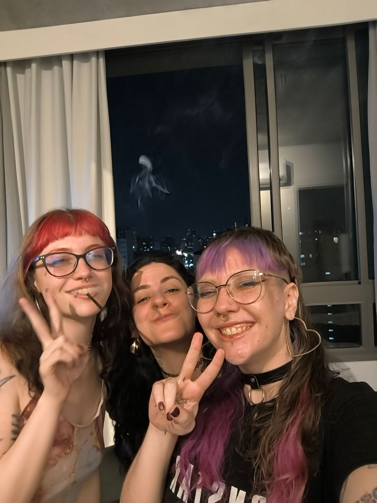 nath Kozlo de franja vermelha fazendo sinal de "dois" com a mão e sorrindo com um Beck na boca, soltando fumaça. nah brisa de cabelo preto também com beck na boca soltando fumaça. eu com franja roxa e pontas do cabelo rosa fazendo 2 com os dedos, sorrindo, a única sem Beck na boca. 