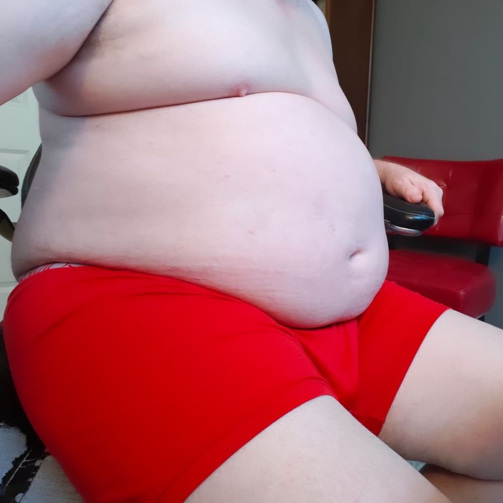 An obese man clad only in red boxer briefs sitting in an office chair.