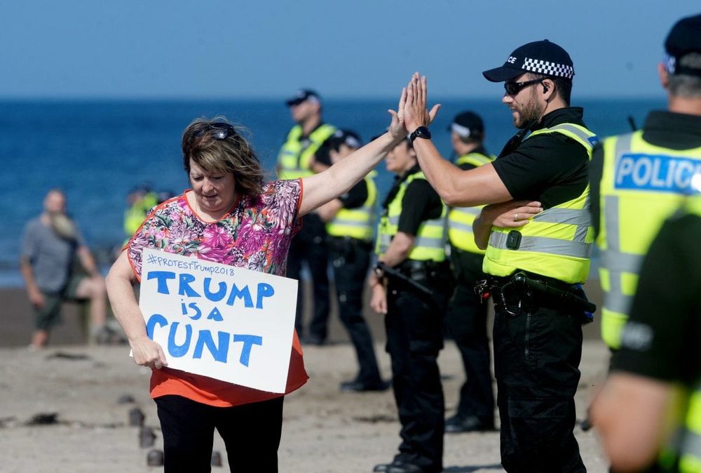 Janey Godley is holding an anti Trump banner, whilst high-fiving a policeman.
