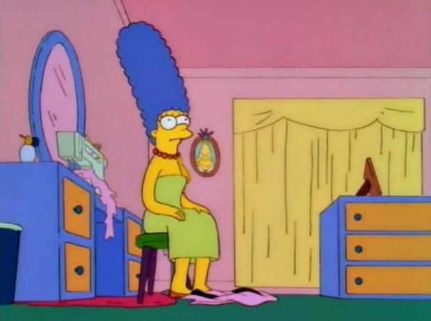 A still of Marge Simpson sitting on stool with her arms on her lap and staring blankly off into space.