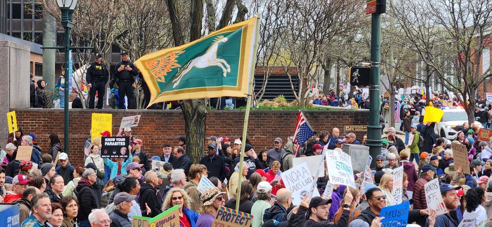 Flying over the marching crowds at the Philadelphia Hands Off protest is a banner with a white horse _proper_, quartered with a sun _gules_, on a field _vert_ with a border  _or_ - the banner of the Rohirrim.