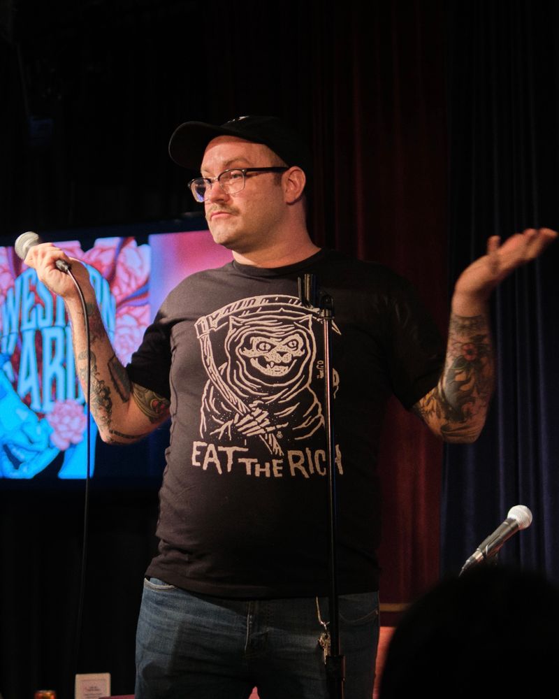 Comedian on stage throwing up his arms in defeat