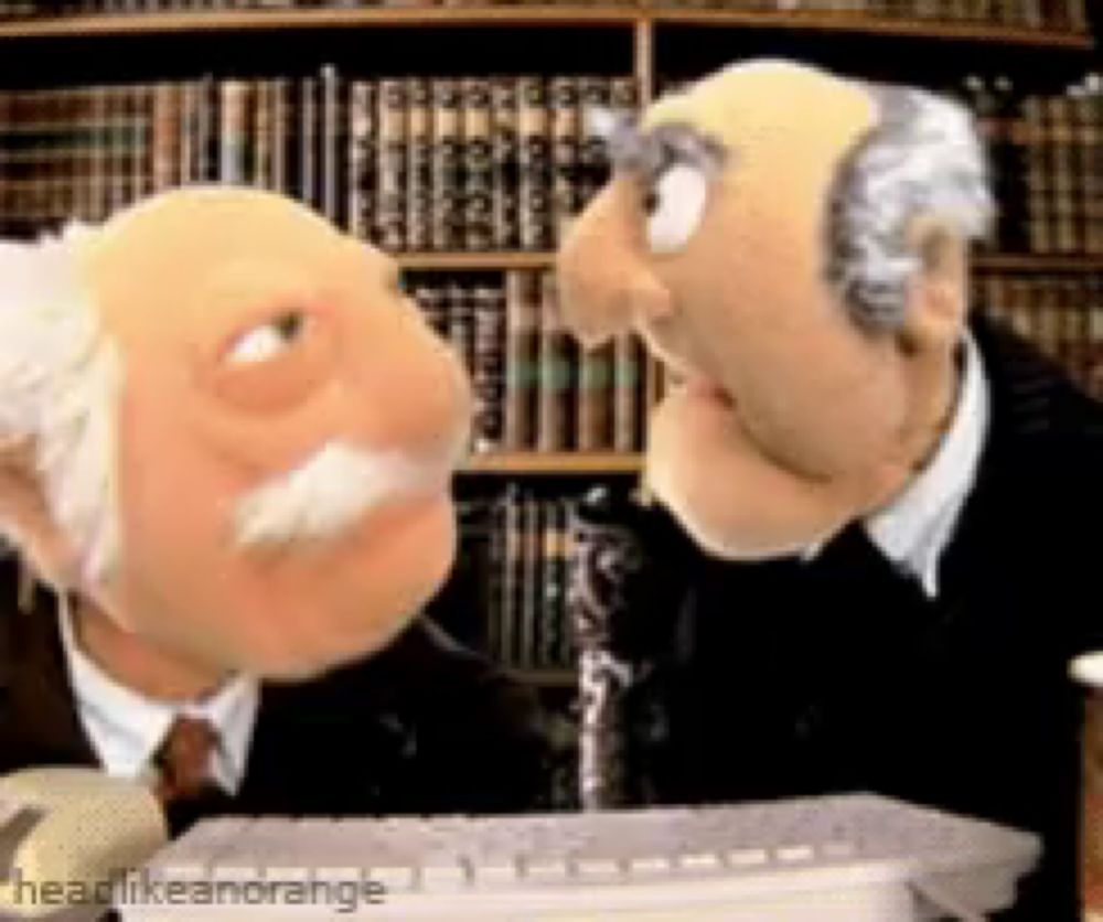 two muppets are talking to each other in front of a bookshelf and a computer keyboard