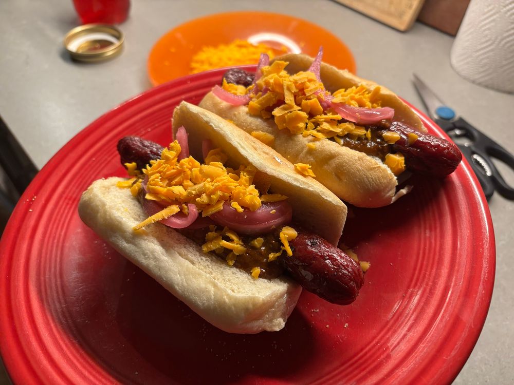 Two hot dogs with chili, pickled red onions and cheddar cheese