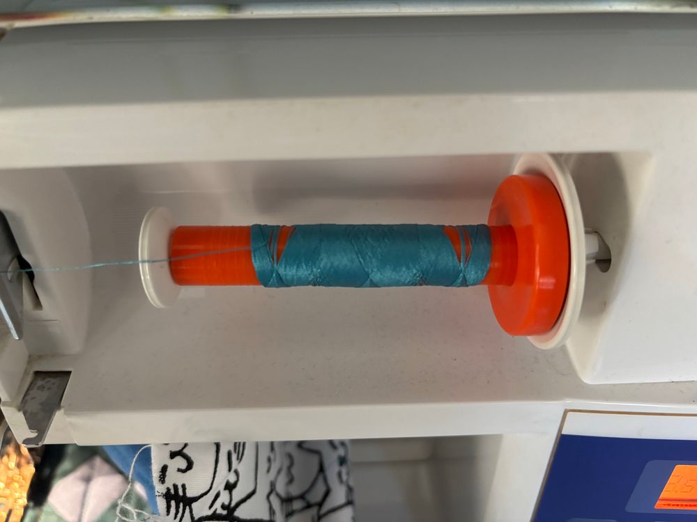 A spool of thread in a sewing machine. There are visible gaps in the thread because there’s so little thread left on the spool. 