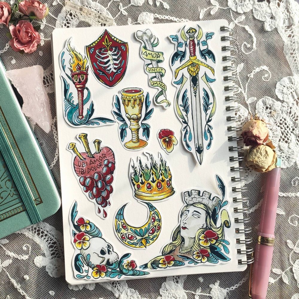 11 stickers with various medieval illustrations. Sleeping princess with pansies, skull of a knight, moon with eyes, burning crown, sacred heart with grape, gold cup, sword, bone with "amor vincit Omnia" shield with a rib cage on it and torch. 