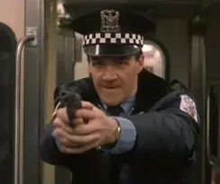 Neil Flynn as a police officer in The Fugitive is pointing a pistol at Harrison Ford's character, Dr. Richard Kimble.