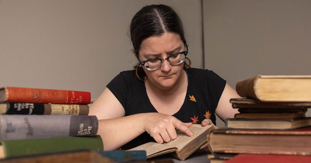 Me looking thoughtfully at an open book I'm holding, pointing to a line of text.  On either side are small piles of old library books.