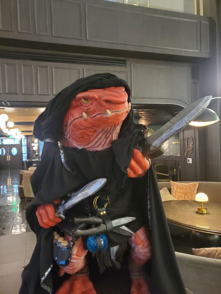 A red skinned fantasy creature in a cloak with short swords