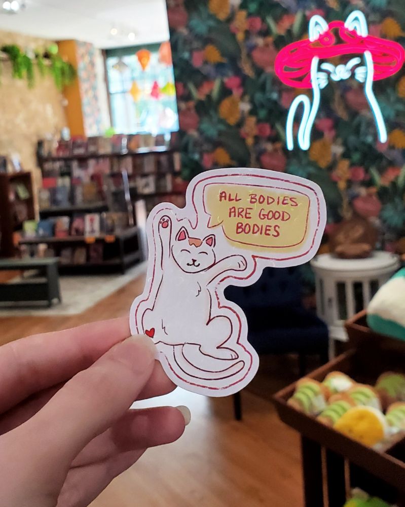 A sticker with a drawing of a cat that says All Bodies Are Good Bodies