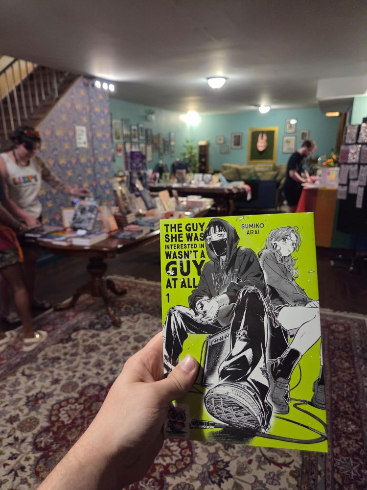 The Guy She Was Interested in Wasn't a Guy at All, Vol. 1 being held by a hand in the Goblin Market Art & Community space during the Queer Book Fair