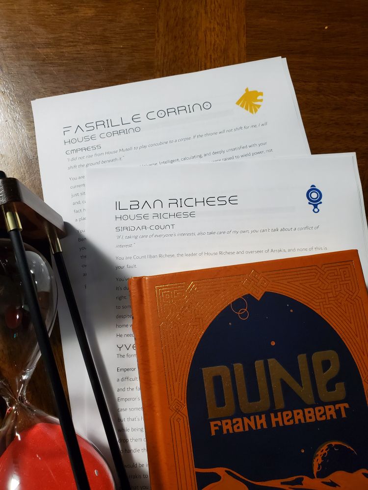 A hardcover of Dune, an hourglass, and a couple character sheets