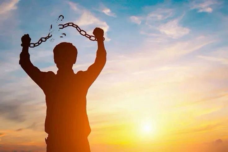 Guy stands in the sunlight wearing chains on his wrists. The chains have shattered.