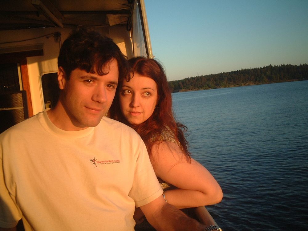 A woman is on a boat a sunset standing next to a man with a white t-shirt