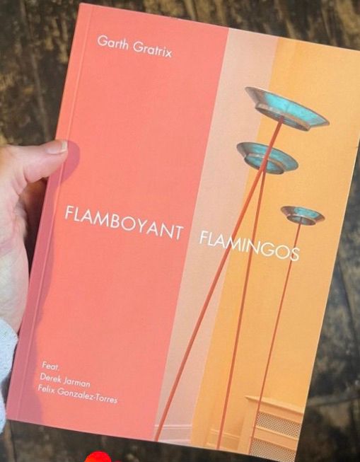 An A5 book in a coral pink and amber yellow stripe cover also showing three bronze spinning plates on metal poles. Image taken by Benjamin Nuttall.

The book is titled Flamboyant Flamingos visible in the middle of the cover in white text. To the top left also in white text is the artists name Garth Gratrix and to the bottom left in white text are two other featured artists names, Felix Gonzalez-Torres and Derek Jarman. 

The book is A5 with 80 pages and self published by Garth Gratrix with an ISBN number. The image depicts the book held in the palm of a hand (Caucasian female hand).



