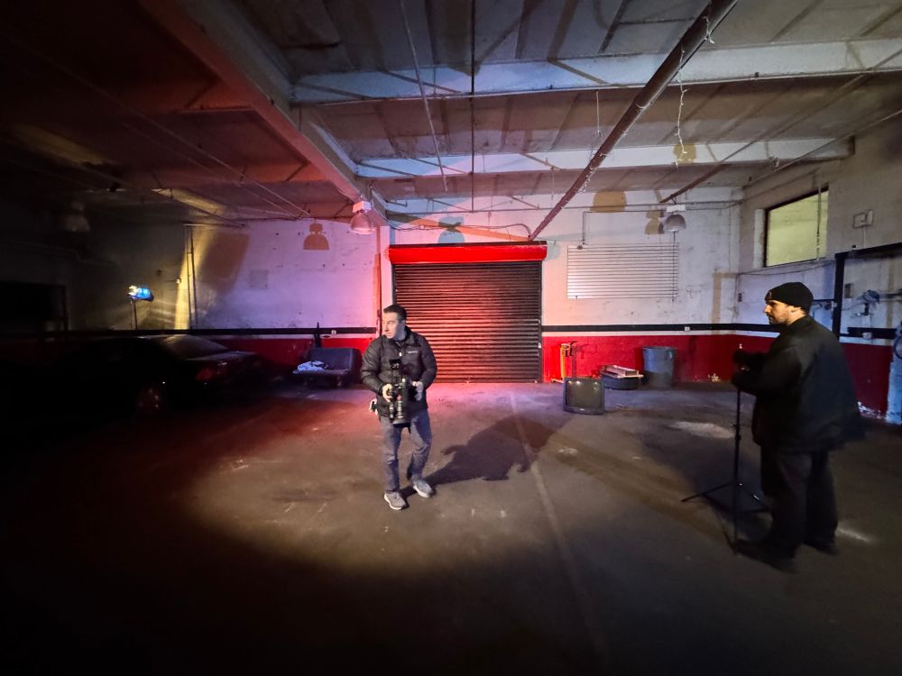 Shot of auto garage, our DO Sal is standing in the center, right in the key light, while I’m standing off to the right, looking like I’m about peace out to go commit a B&E.