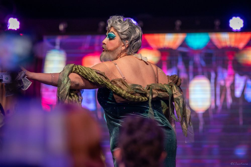 Photo of me dressed as Calypso. My back is to the camera and my face is in profile as I reach to accept a tip from an audience member (offscreen)