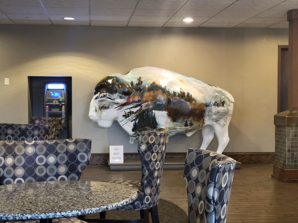 ATM machine next to white bison with painted mountain scene on its Flank. 
