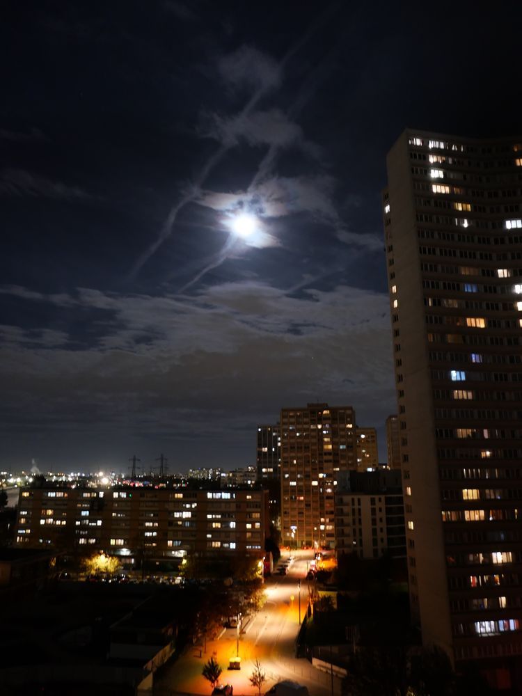 La pleine lune ou environ vue de ma fenêtre, près des tours aux fenêtres allumées et de l'éclairage urbain rose orangé 
