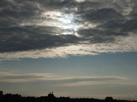 Le soleil aperçu dans une couche de nuages furieux, le ciel plus dégagé en dessous, les faîtes des toits parisiens, en bas