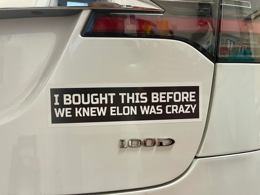 A photo of a bumper sticker on a Tesla that says “I bought this before we knew Elon was crazy “ 