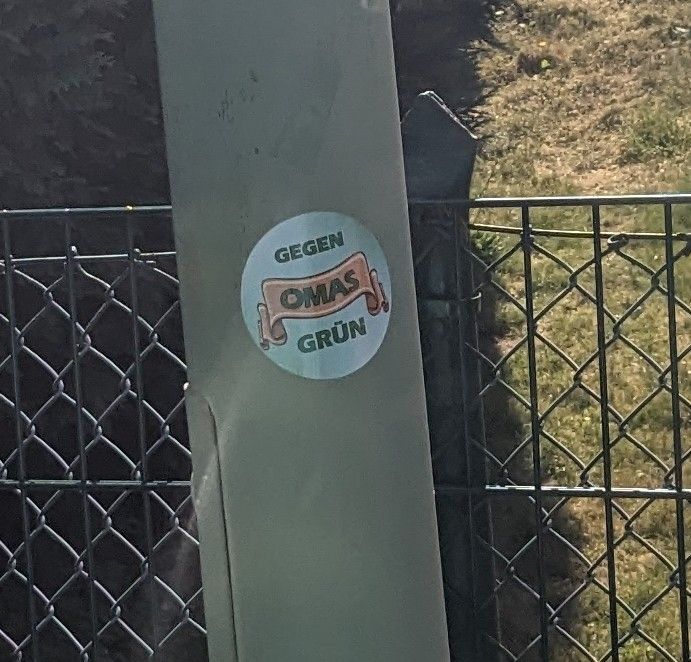 Ein runder Sticker von "Omas gegen grün" klebt an einer Laterne. 