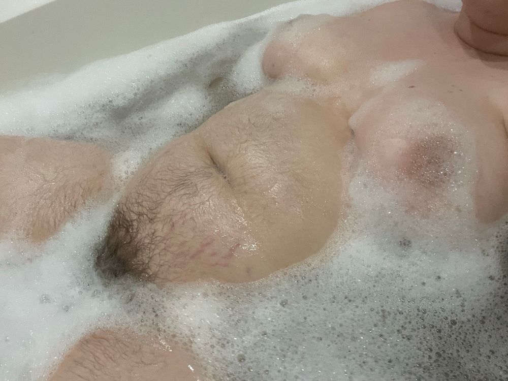 another picture of ty in the bath from slightly further away. his body is surrounded by small bubbles with all of his hairy tummy exposed. there are some bubbles between his thighs and on his tits.