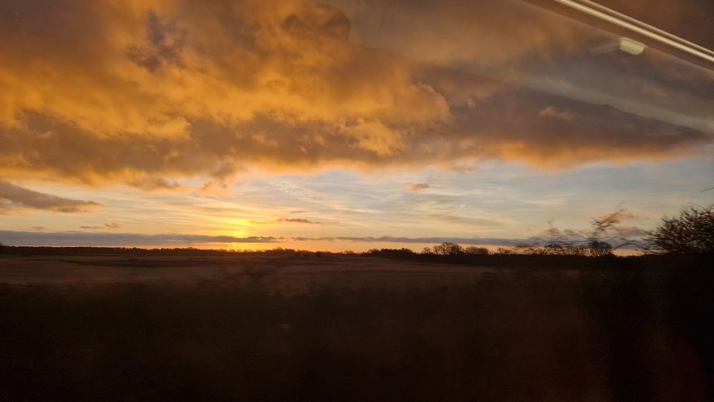 a sun hangs low over fields as it rises, colouring the clouds above it a deep, rich orange