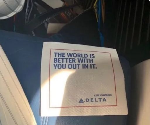 A cocktail napkin from Delta Airlines that has a note: "The world is better with you out in in." Because of the formatting, it's easy to misread this as "The world is better without you in it."