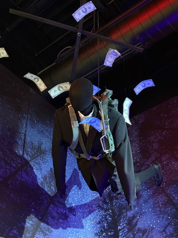 Suspended mannequin representing D.B. Cooper with floating currency falling around him. 