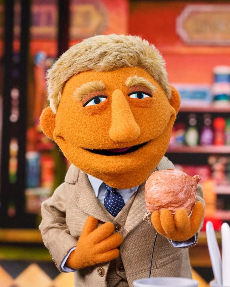 And orange, humanoid muppet with a large nose, short blond hair, and bushy blond eyebrows. He's wearing a tie and a beige detective trenchcoat and holding a pinky-brown blob that may be....ice cream? A brain?