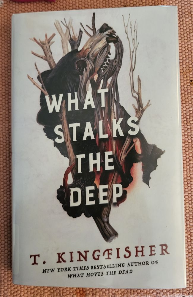 Cover of "What stalks the deep" by T. Kingfisher. A partially decayed  bear wrapped through dead tree branches.