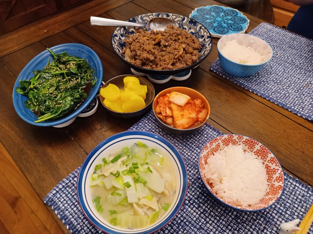 A dinner spread with spinach, ground beef bulgogi, yellow pickled radish, kimchi, pale green cabbage and dumpling soup, and rice.
