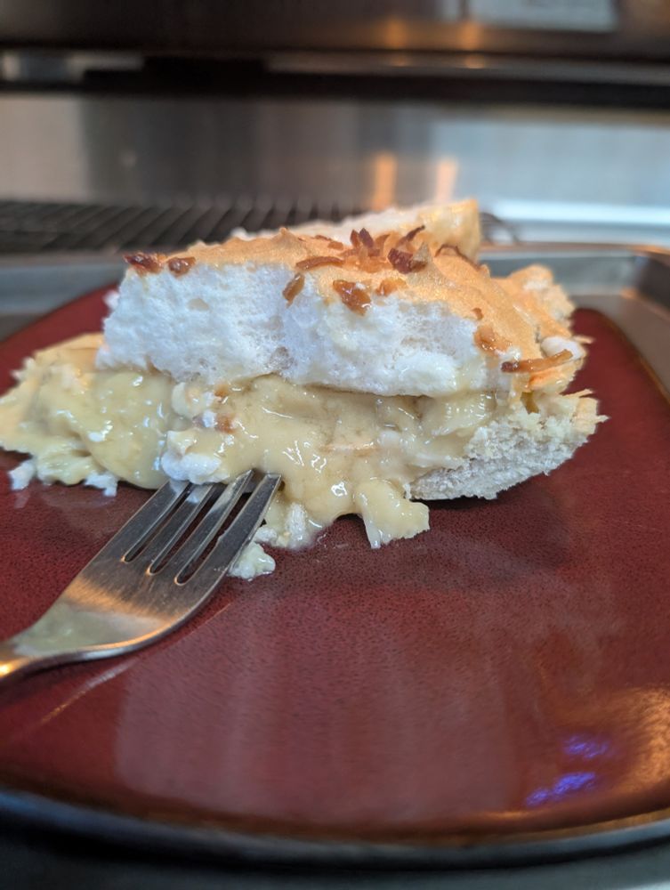 A coconut cream pie with meringue topped with coconut on a red and black plate with a fork 