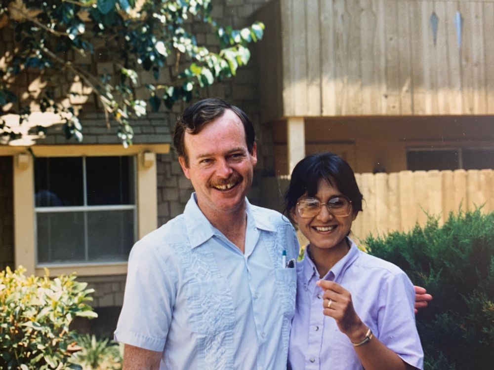A young man and woman stand outside an apartment building and smile