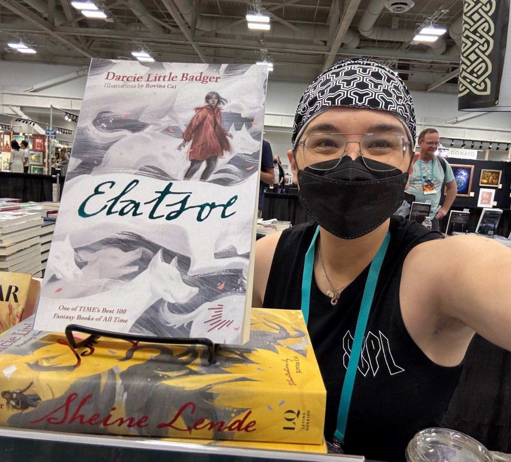 Darcie sits at a table and takes a selfie in front of her books