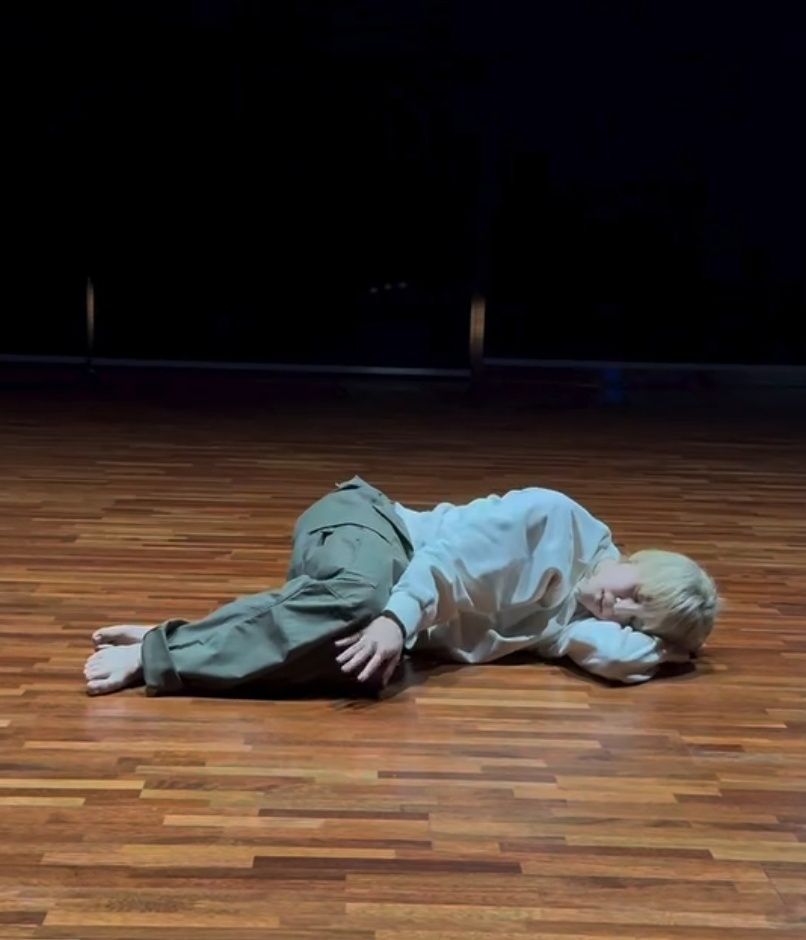 Park Jimin of BTS lying down on a wooden floor, his eyes closed like he's sleeping.