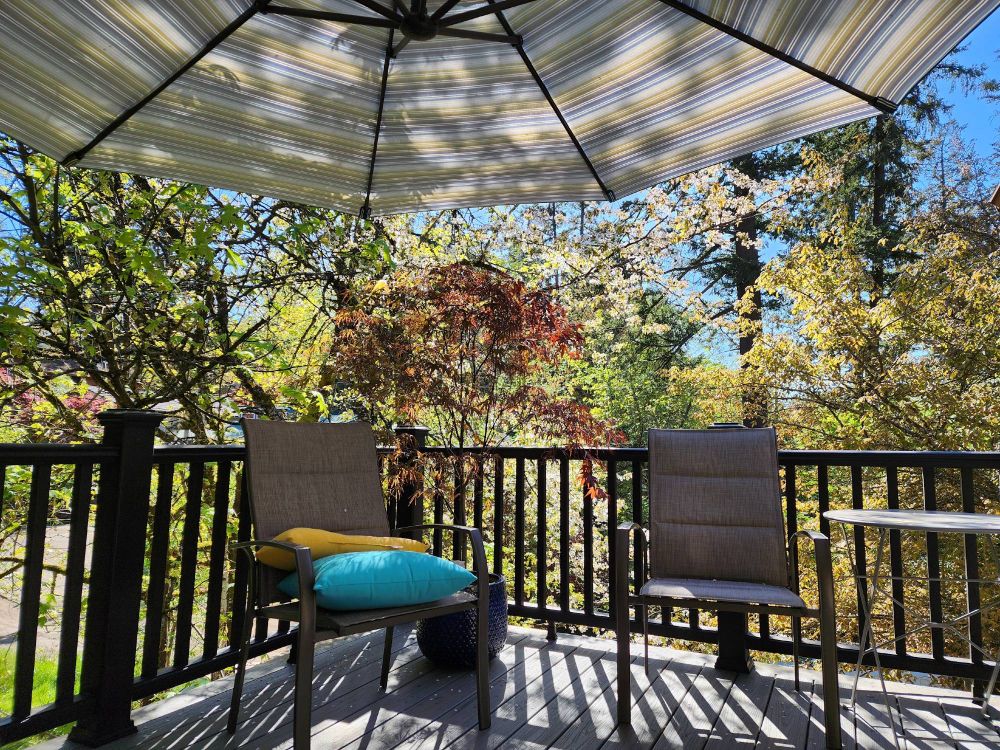 A sun dappled deck surrounded by colorful, blooming trees and protected by a large striped umbrella. Heaven!