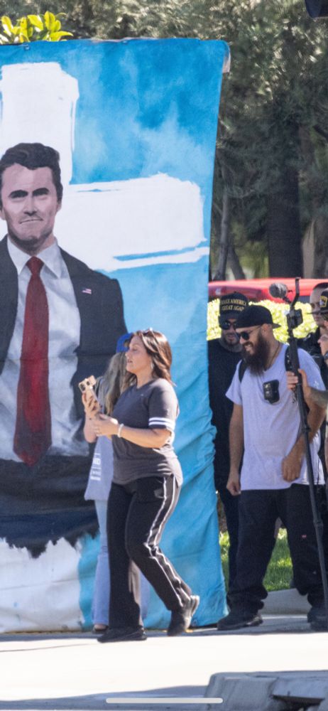 Julie Turcol and Chris Reyes, who is closely associated with the Proud Boys, flew to SoCal from Portland last week to participate in “ Security “ for VOTE PRAY STAND at Calvary Chapel in Chino. They are sitting here, in front of Calvary Chapel,with a giant painting of Charlie Kirk, which Chris created.