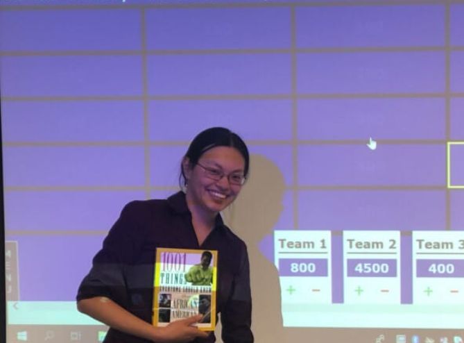 me, East Asian woman, holding 1001 Things Everyone Should Know About African American History, with the scores behind me. Team 1: 800. Team 2: 4500. Team 3: 400