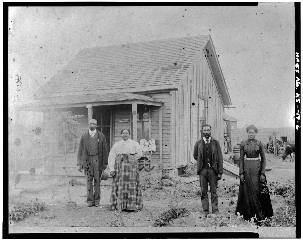 Two women in long skirts & two men in suits in front of their home. Library of Congress Prints and Photographs Division.